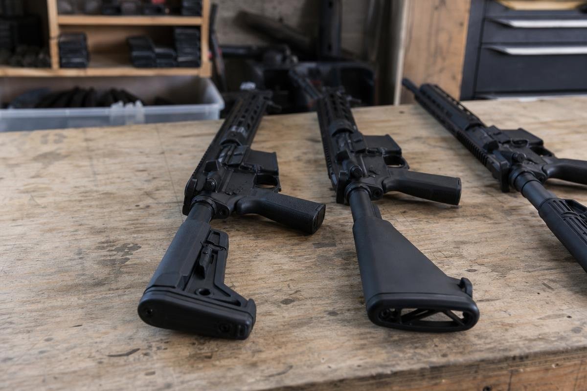 Three AR-15 rifles with different stock types resting on a wooden workbench.