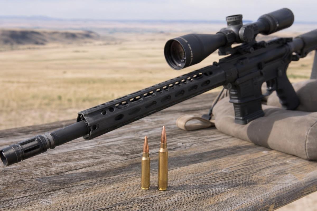 A long-range rifle with a scope resting on a shooting bag with two cartridges standing in the foreground.