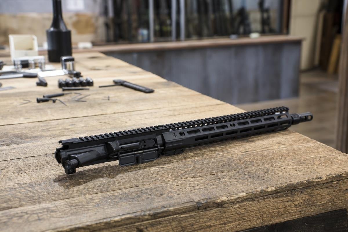 An assembled AR-15 upper receiver resting on a wooden workbench.