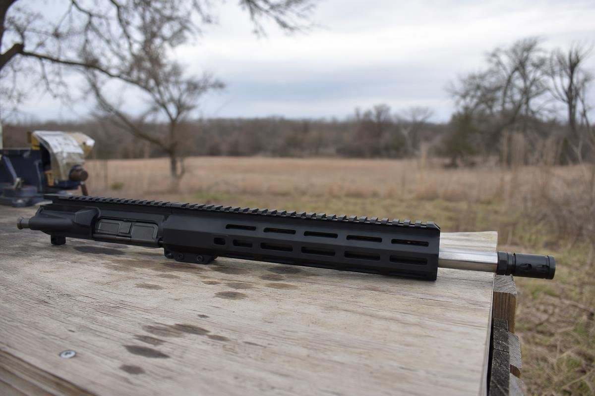 An AR-15 upper receiver assembly resting on a wooden surface outdoors.
