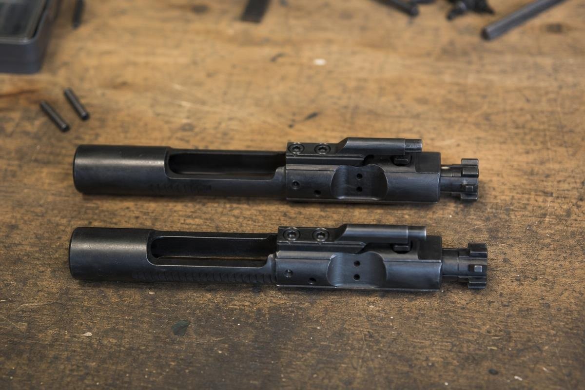 Two bolt carrier groups side by side on a wooden workbench.