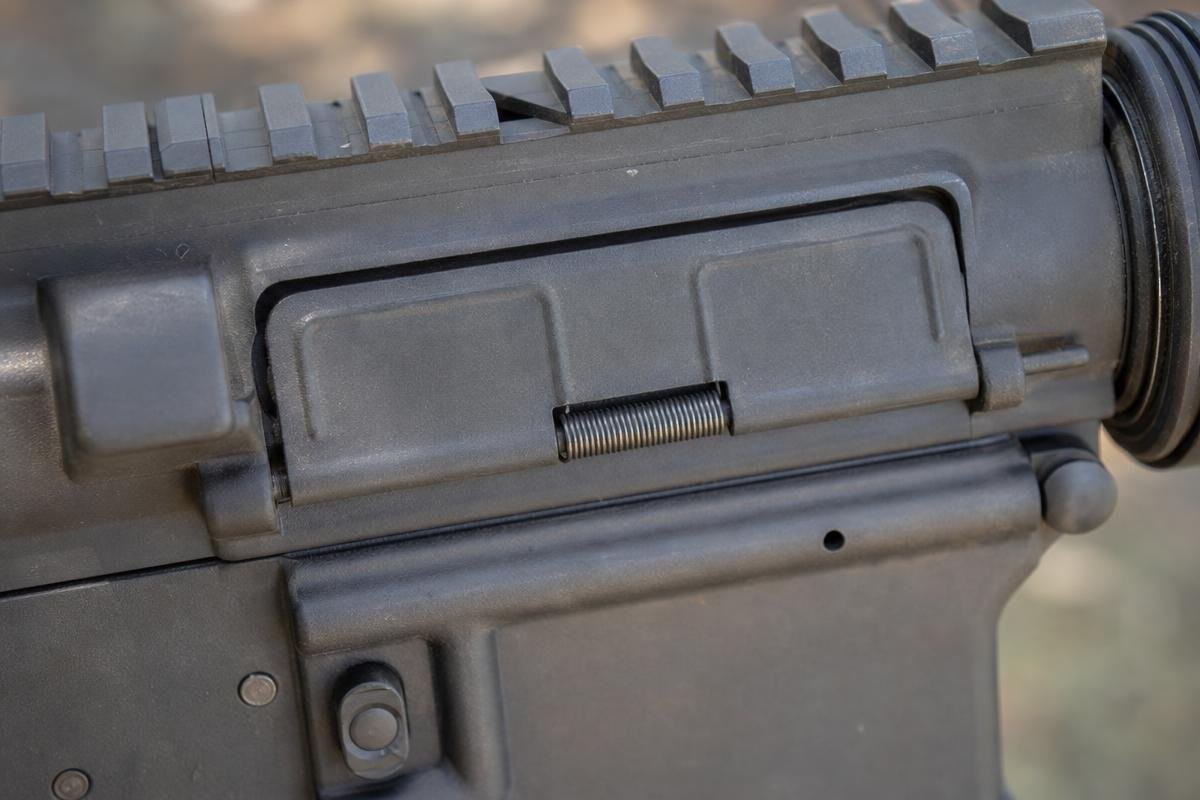 Close-up of an AR-15 dust cover installed on the ejection port of a rifle.