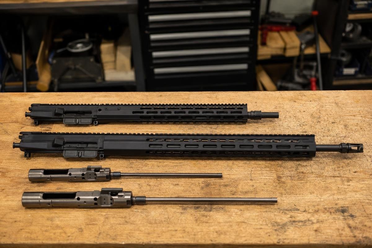 Two AR-style upper receivers and bolt carrier groups laid out on a wooden workbench.