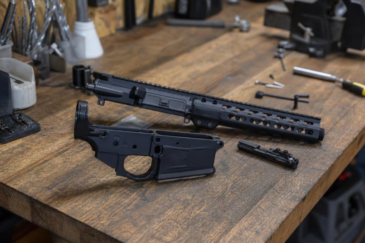 An AR-10 upper receiver, lower receiver, and assembly tools laid out on a wooden workbench.