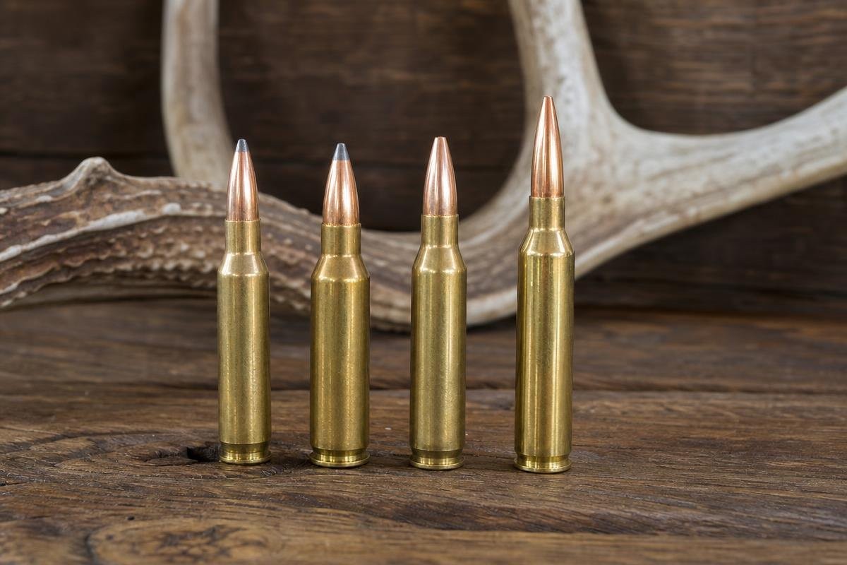 Four rifle cartridges standing in a row against a wooden background with antlers.