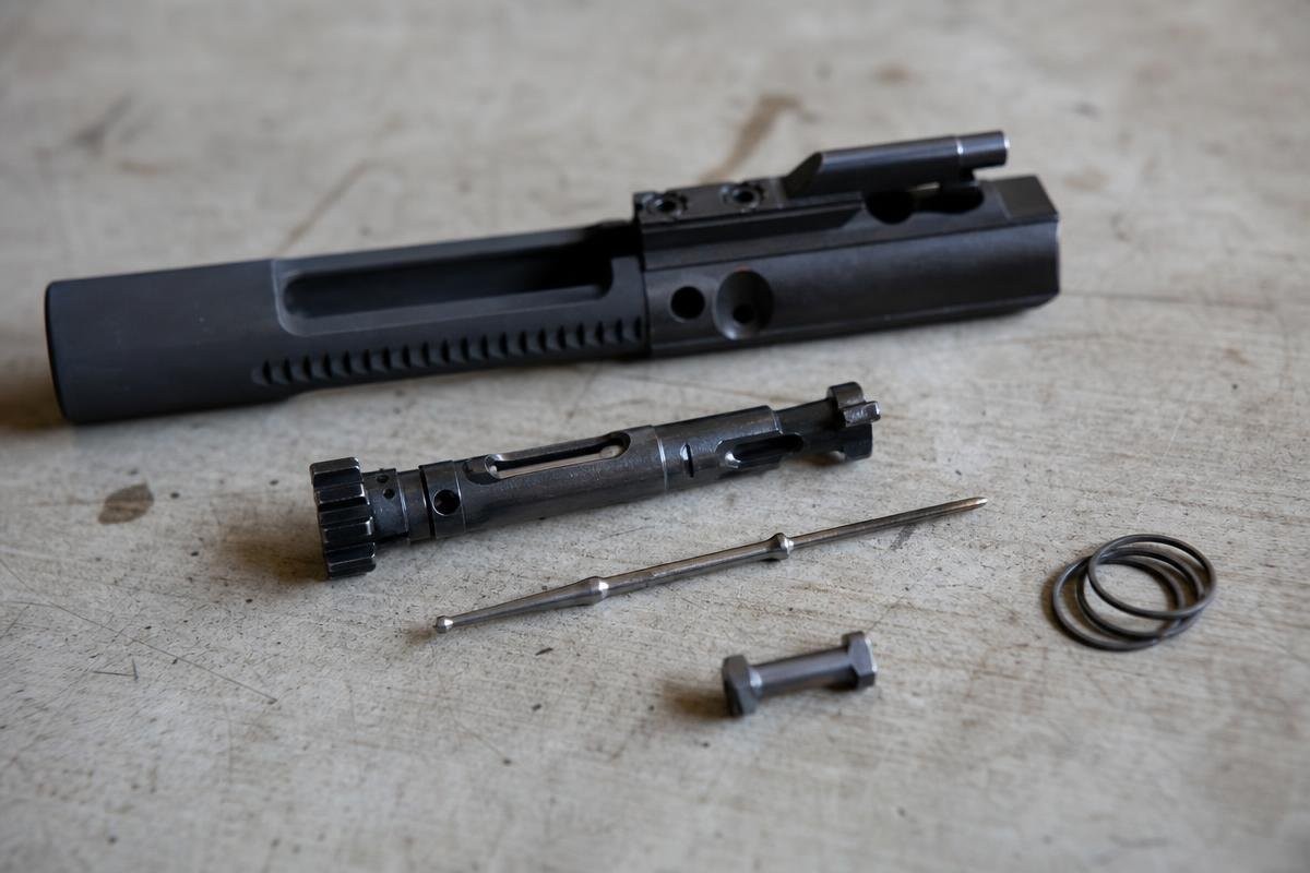 A disassembled AR-15 bolt carrier group showing the carrier, bolt, firing pin, cam pin, and extractor spring.
