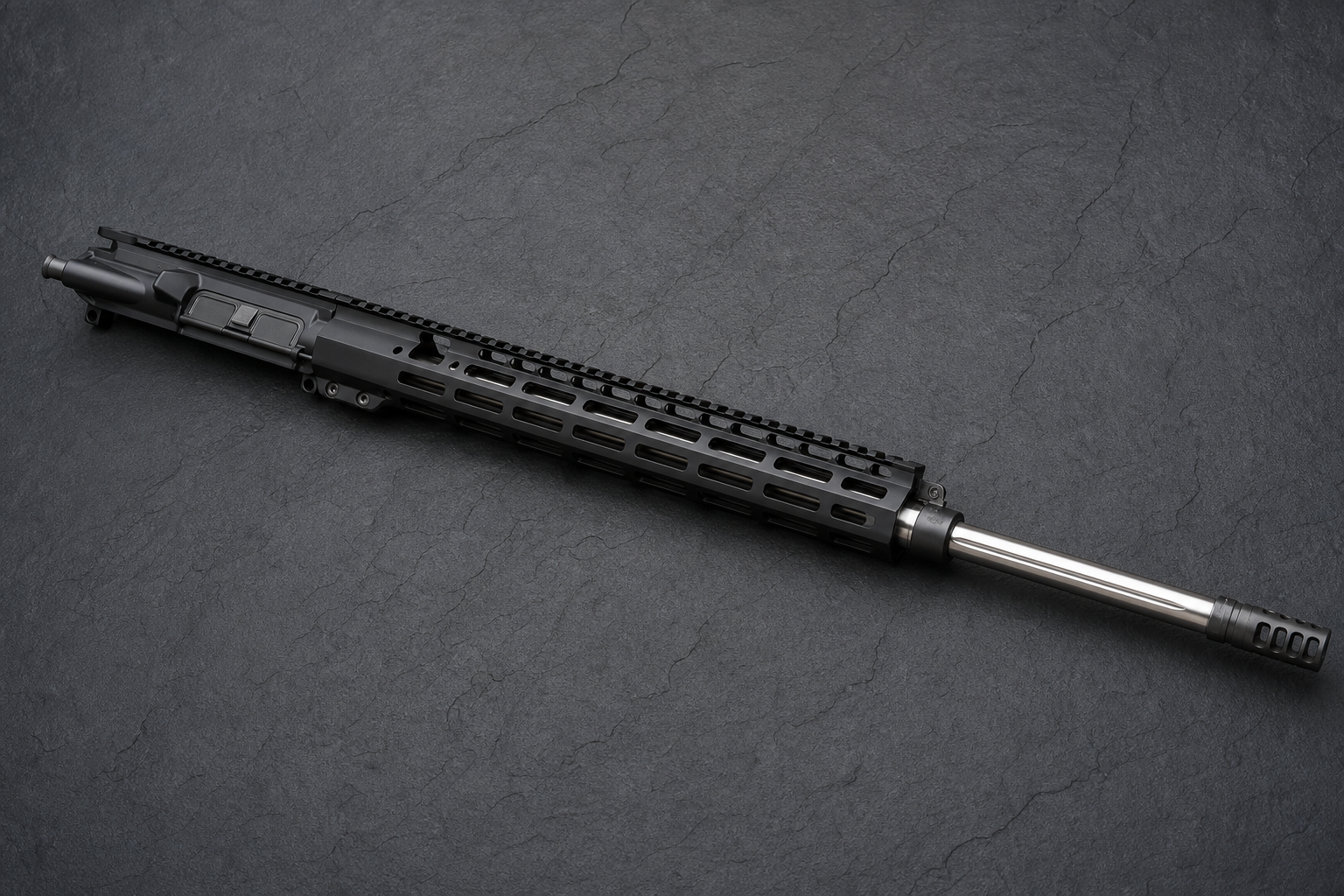 A long-barreled black AR-15 upper receiver with a full-length M-LOK handguard, stainless fluted barrel, and muzzle brake resting on dark slate.