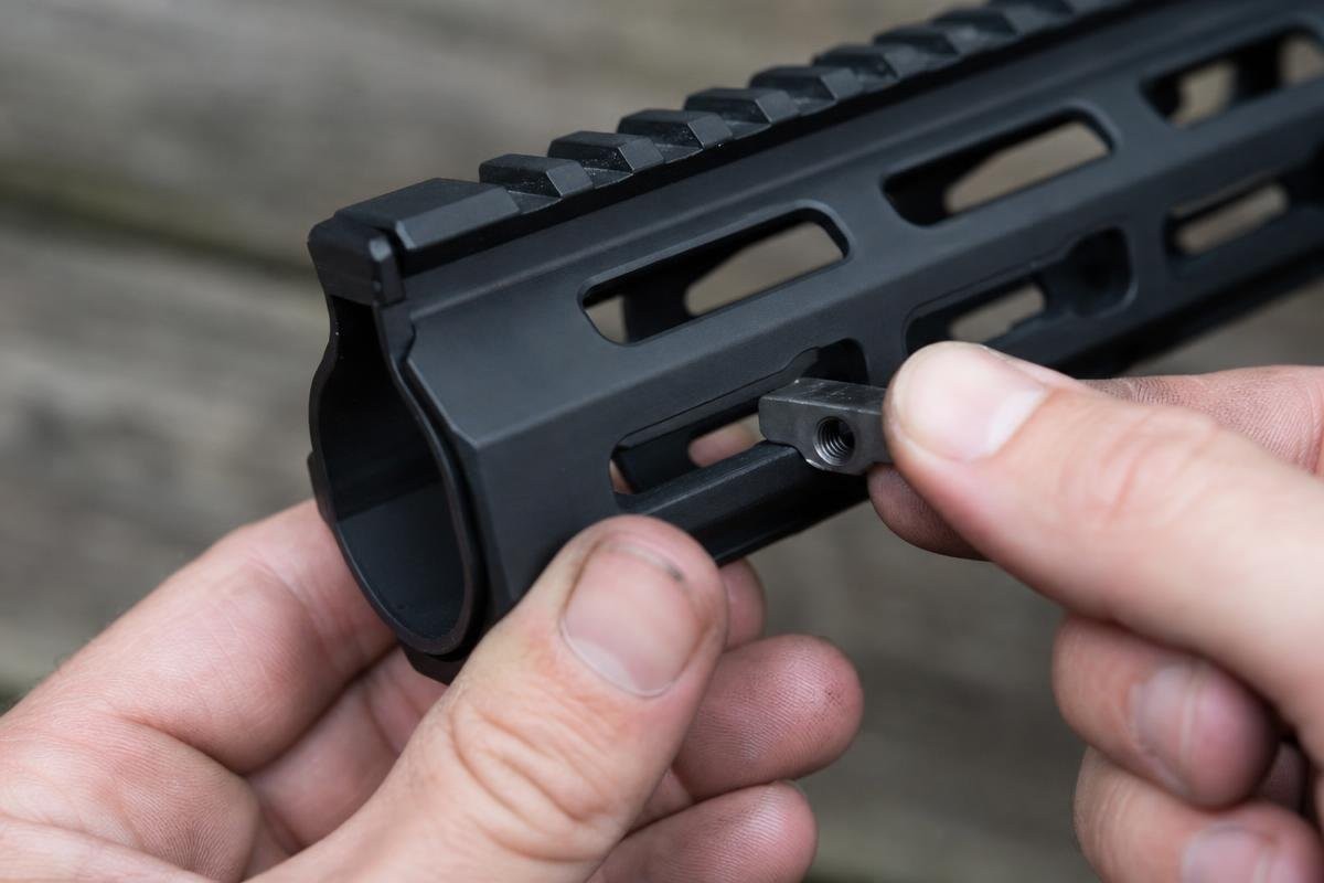 A hand holding a T-nut against a rectangular slot on an M-LOK handguard.