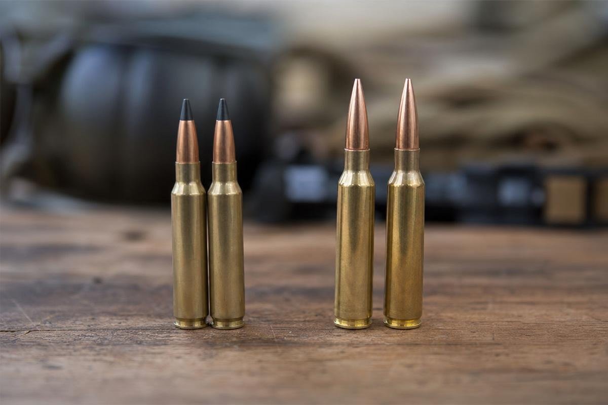 Two 224 Valkyrie cartridges standing next to two 6.5 Creedmoor cartridges on a wooden surface.