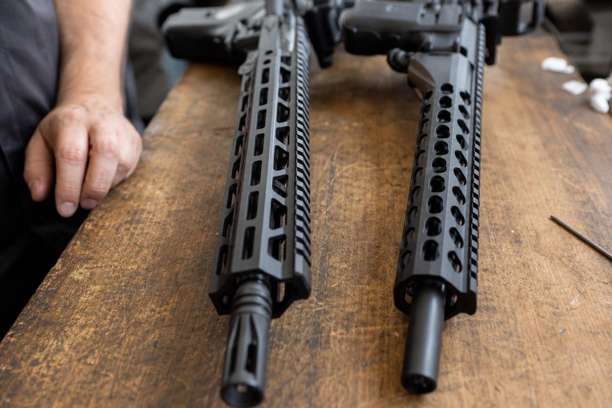 Two AR-15 handguards with different mounting slot patterns resting on a wooden workbench.
