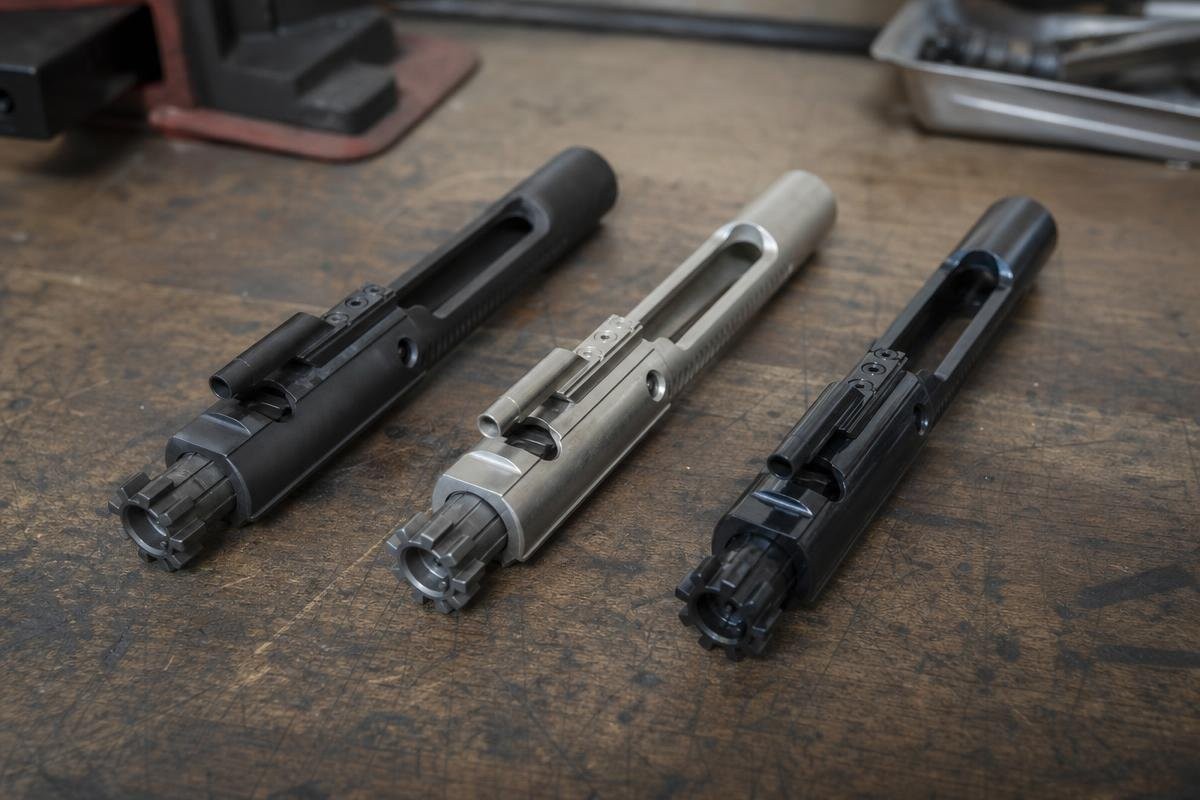 Three bolt carrier groups with different surface finishes laid out on a workbench.