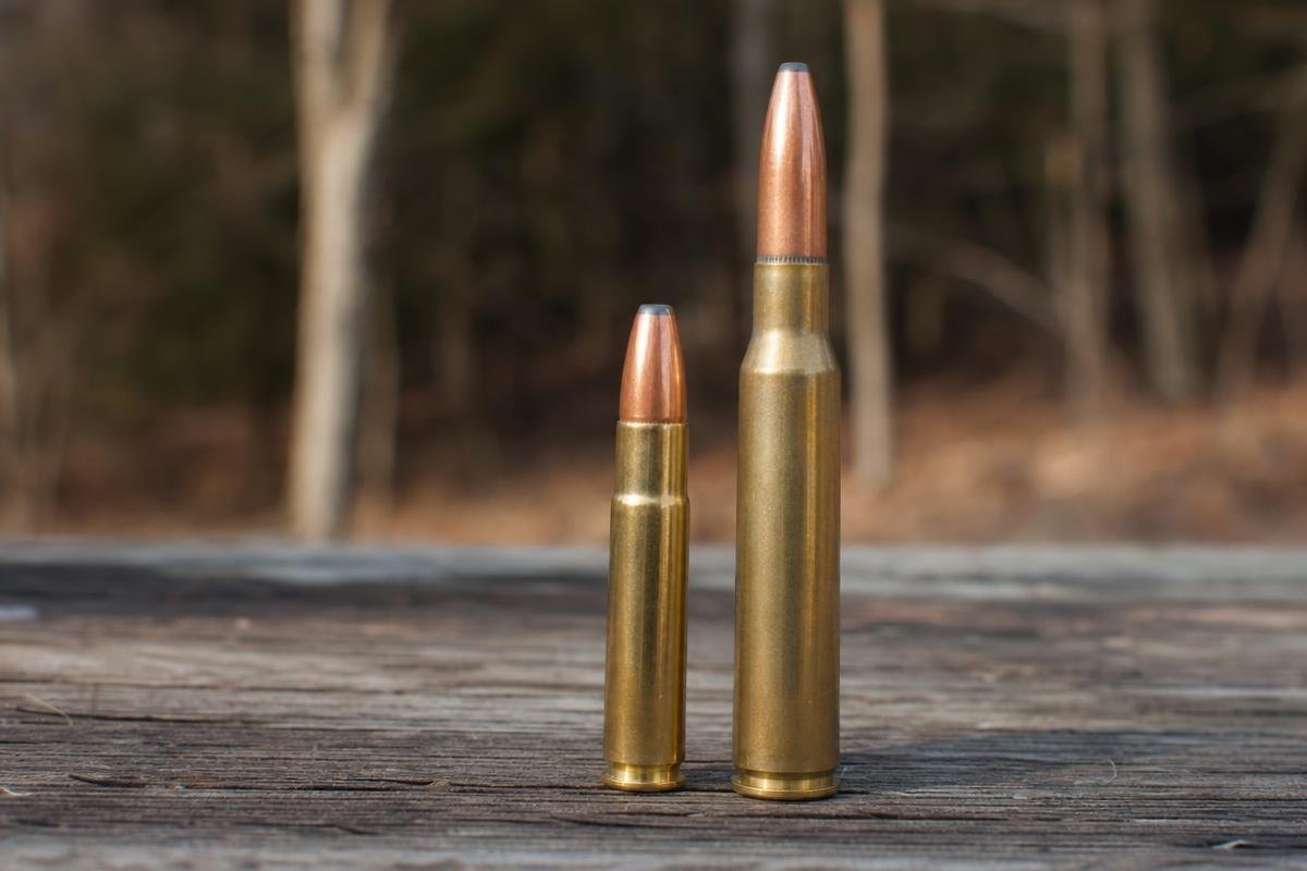 A 350 Legend cartridge standing next to a 30-30 Winchester cartridge on a wooden surface.