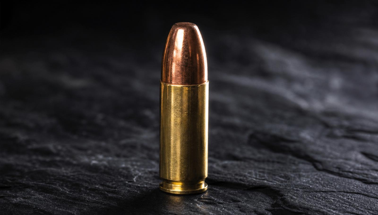 A single .350 Legend straight-walled rifle cartridge standing upright on dark slate.