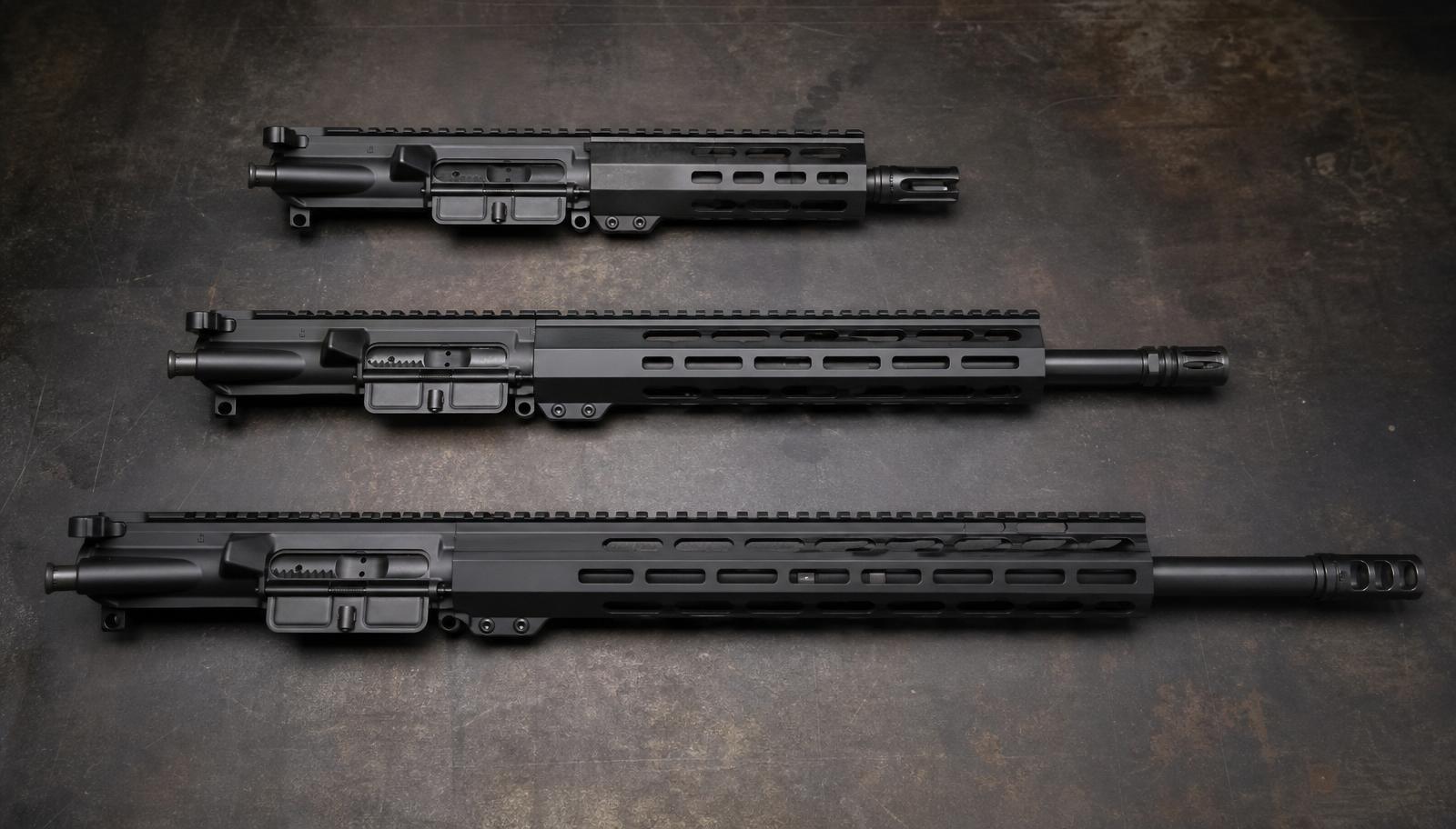 Three AR-15 complete uppers arranged in a row on a dark workbench, showing short defensive, mid-length range, and long precision configurations.