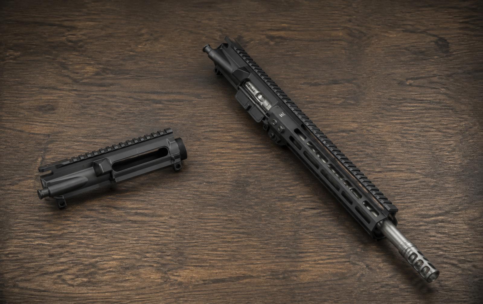 A bare stripped AR-15 upper receiver next to a fully assembled complete upper with 16-inch barrel, M-LOK handguard, and muzzle brake on a dark walnut workbench.